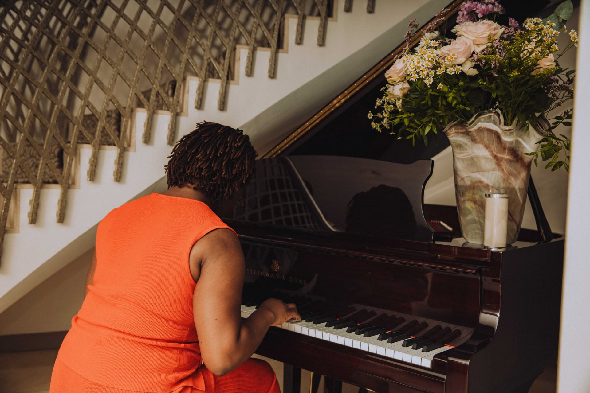 A pianist playing a Steinway grand beside a sculptural staircase and floral arrangement