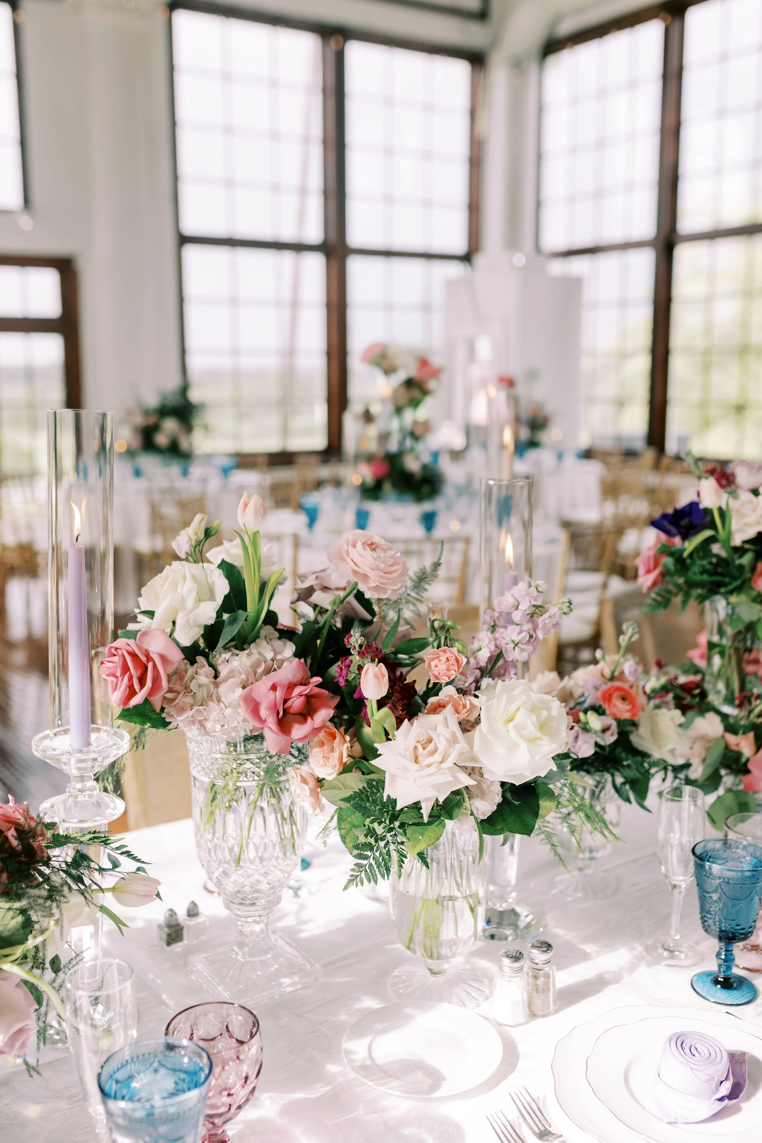 Close detail of a place setting with cobalt glassware, pale florals and taper candles