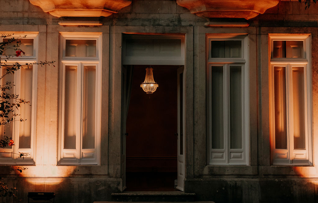 A candlelit palace doorway at dusk, a crystal chandelier glowing within warm uplit stone shutters