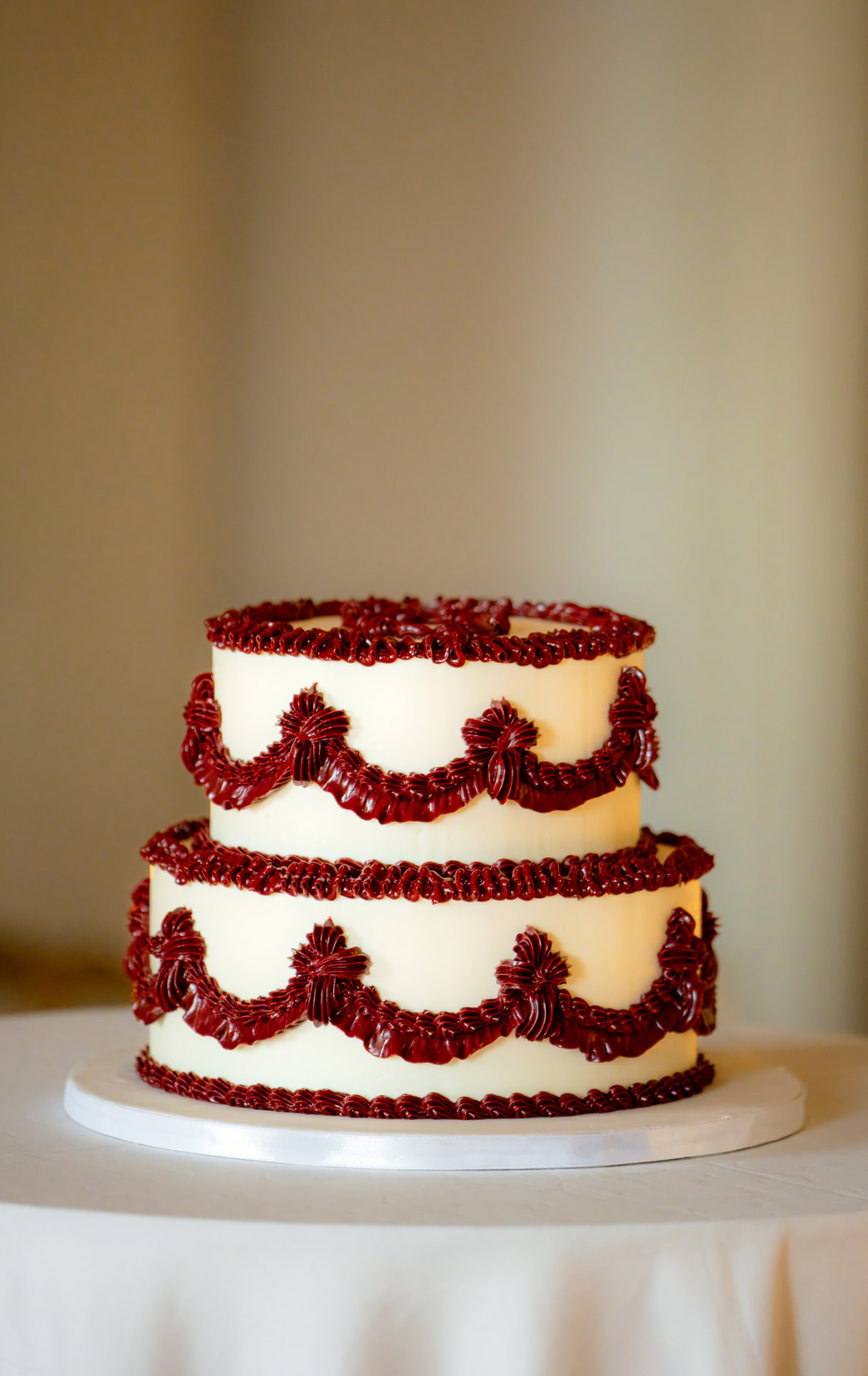 Two-tier ivory cake with burgundy piped scallops and bows on a linen-draped table