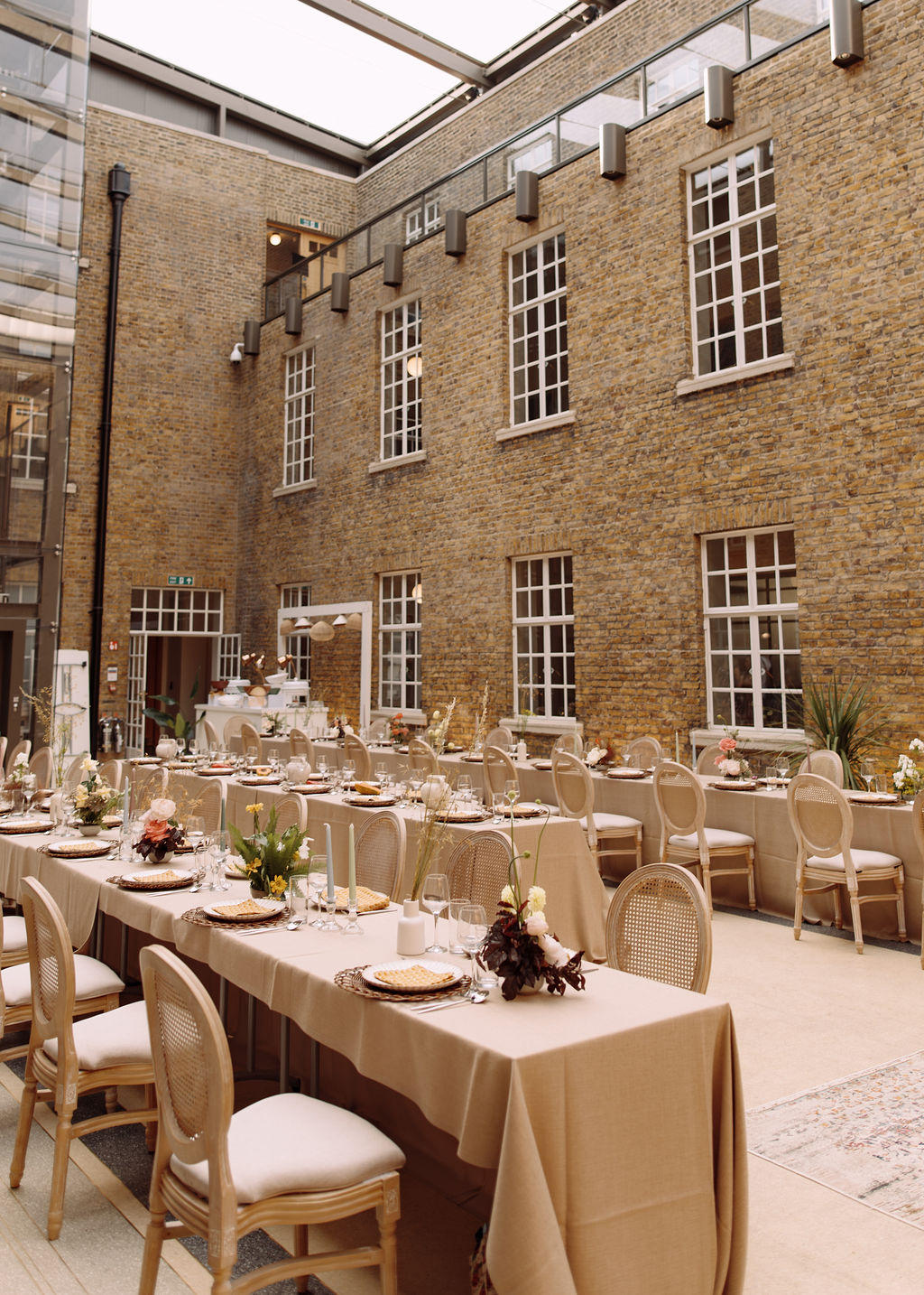 Brick atrium under a glass roof with long linen tables and cane chairs