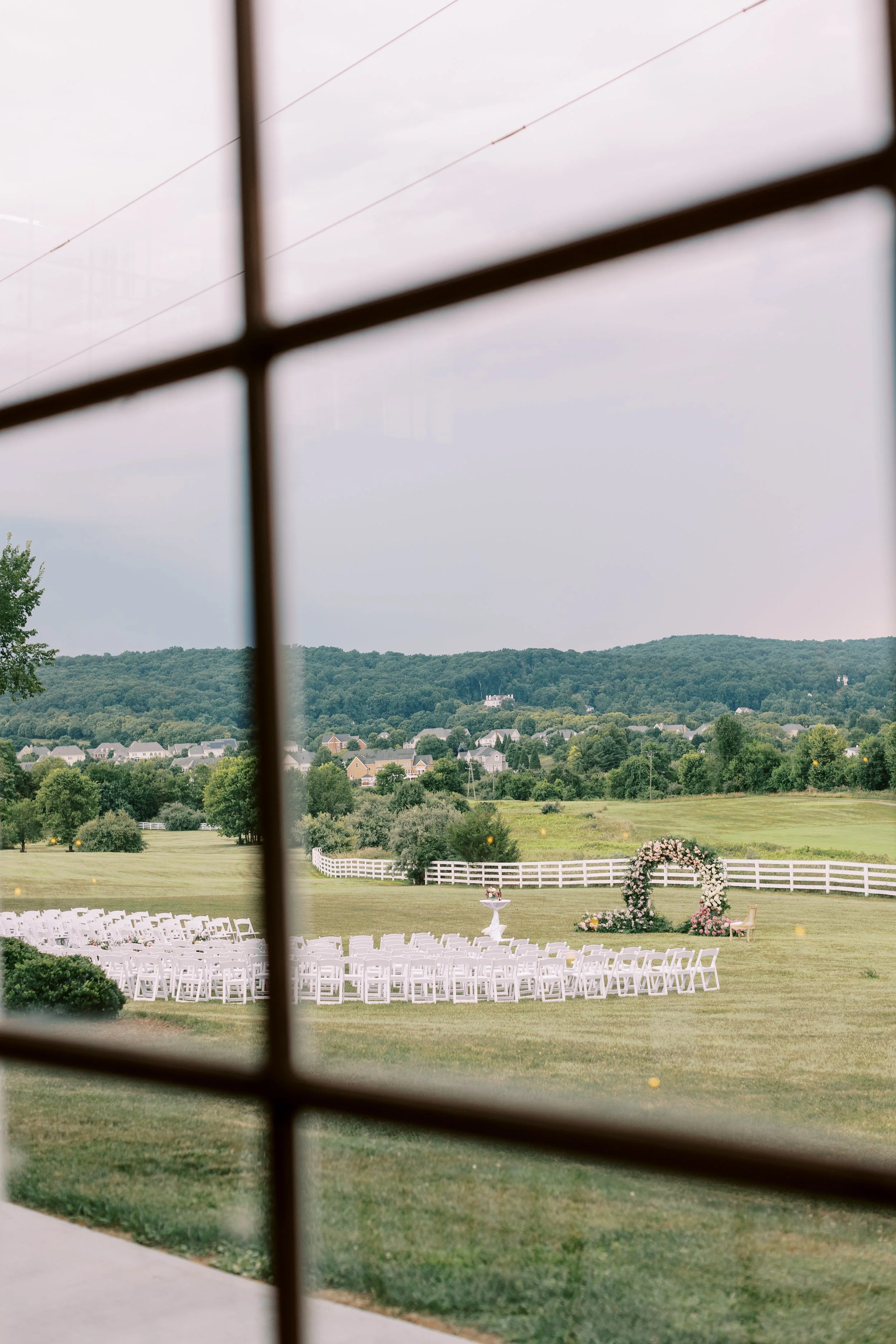 Ceremony lawn and floral arch seen through a steel framed window from inside the manor