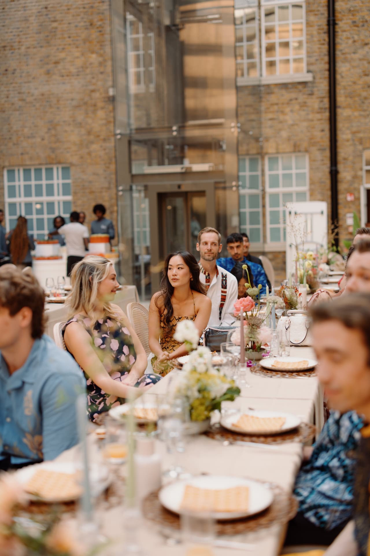 Guests seated along a long courtyard table with candles and garden florals under a brick atrium