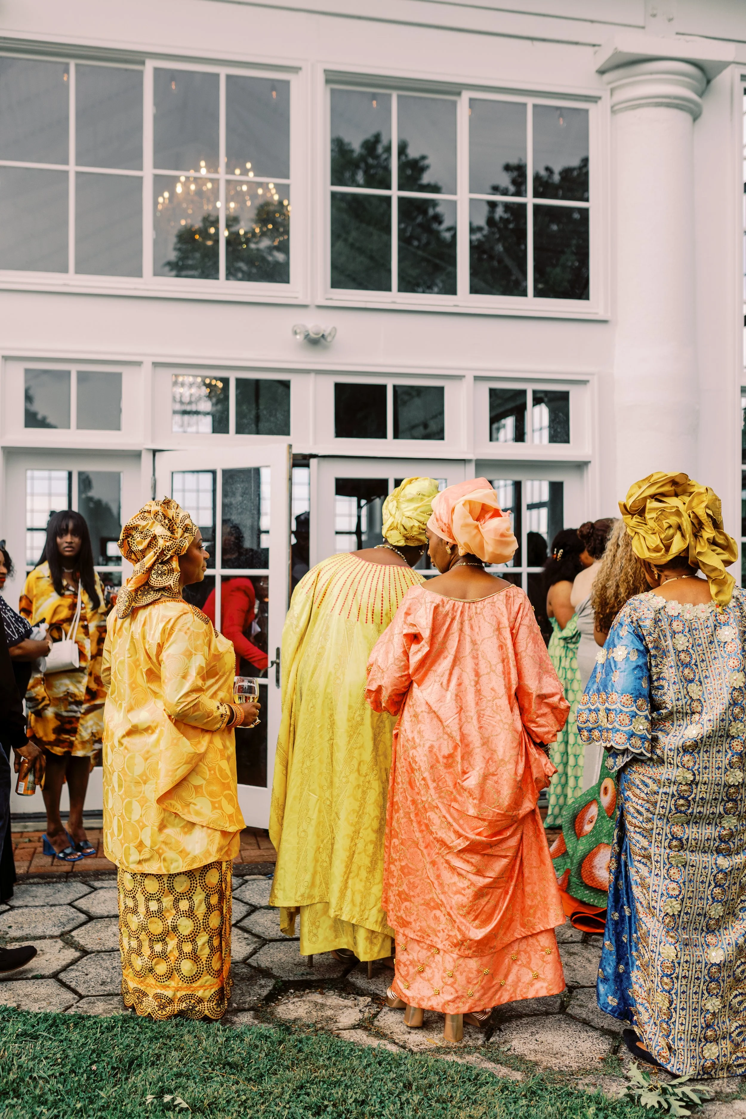 Guests in brightly coloured gele head wraps and lace gowns gathered outside the manor