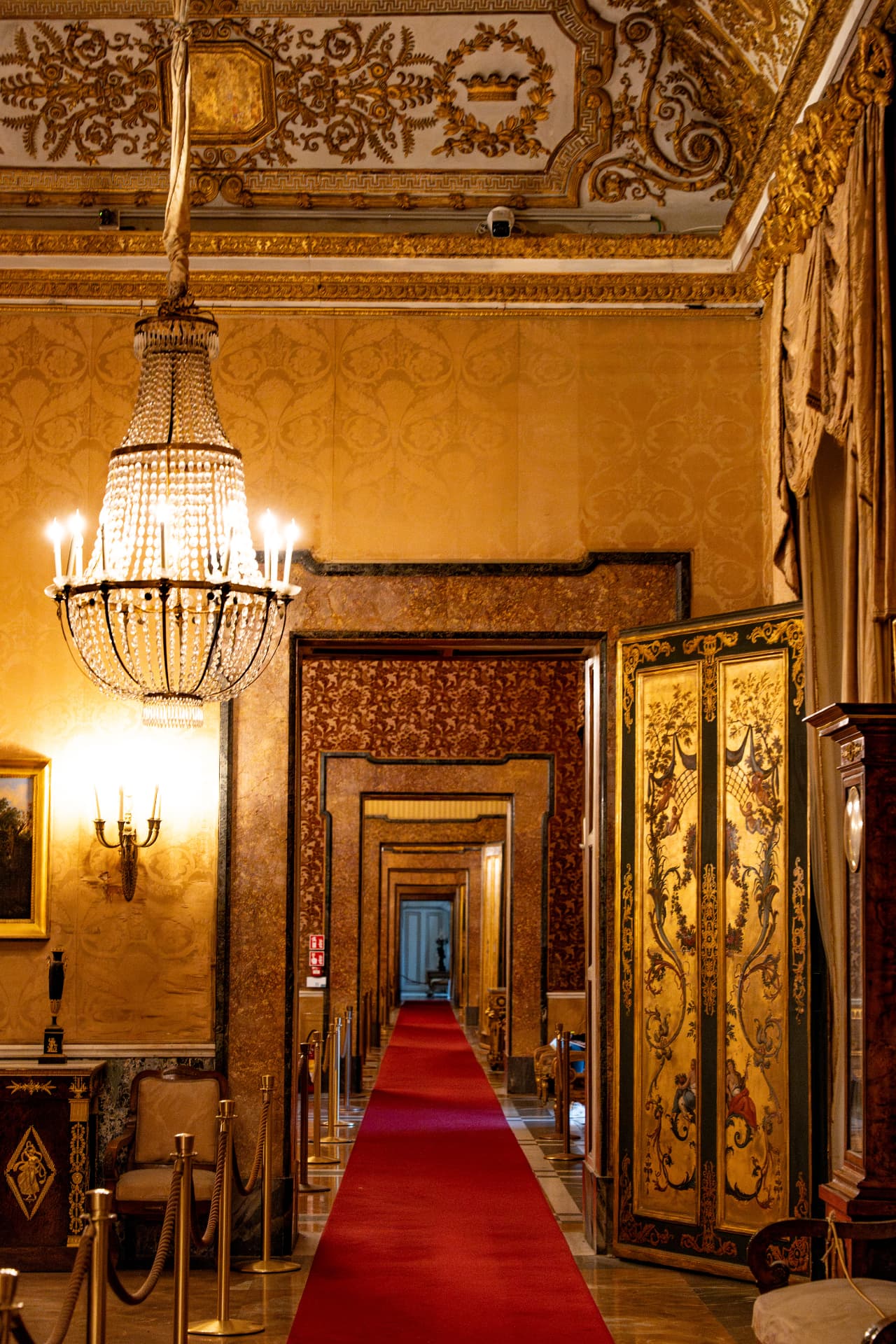 Gilded palace enfilade in Naples with crystal chandelier and red carpet running through successive doorways