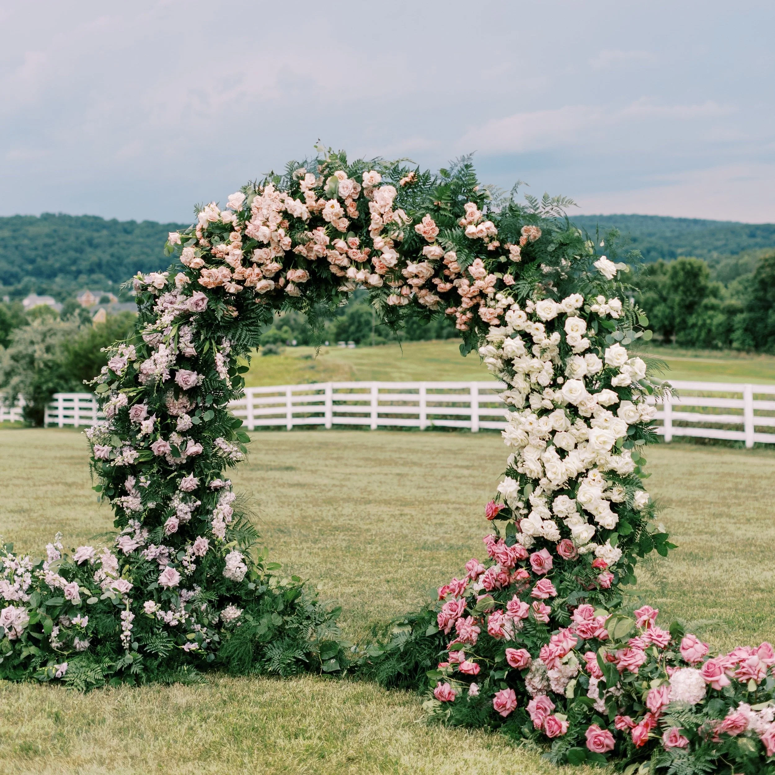 Blush and white floral ceremony arch standing on estate lawns with the Virginia hills behind