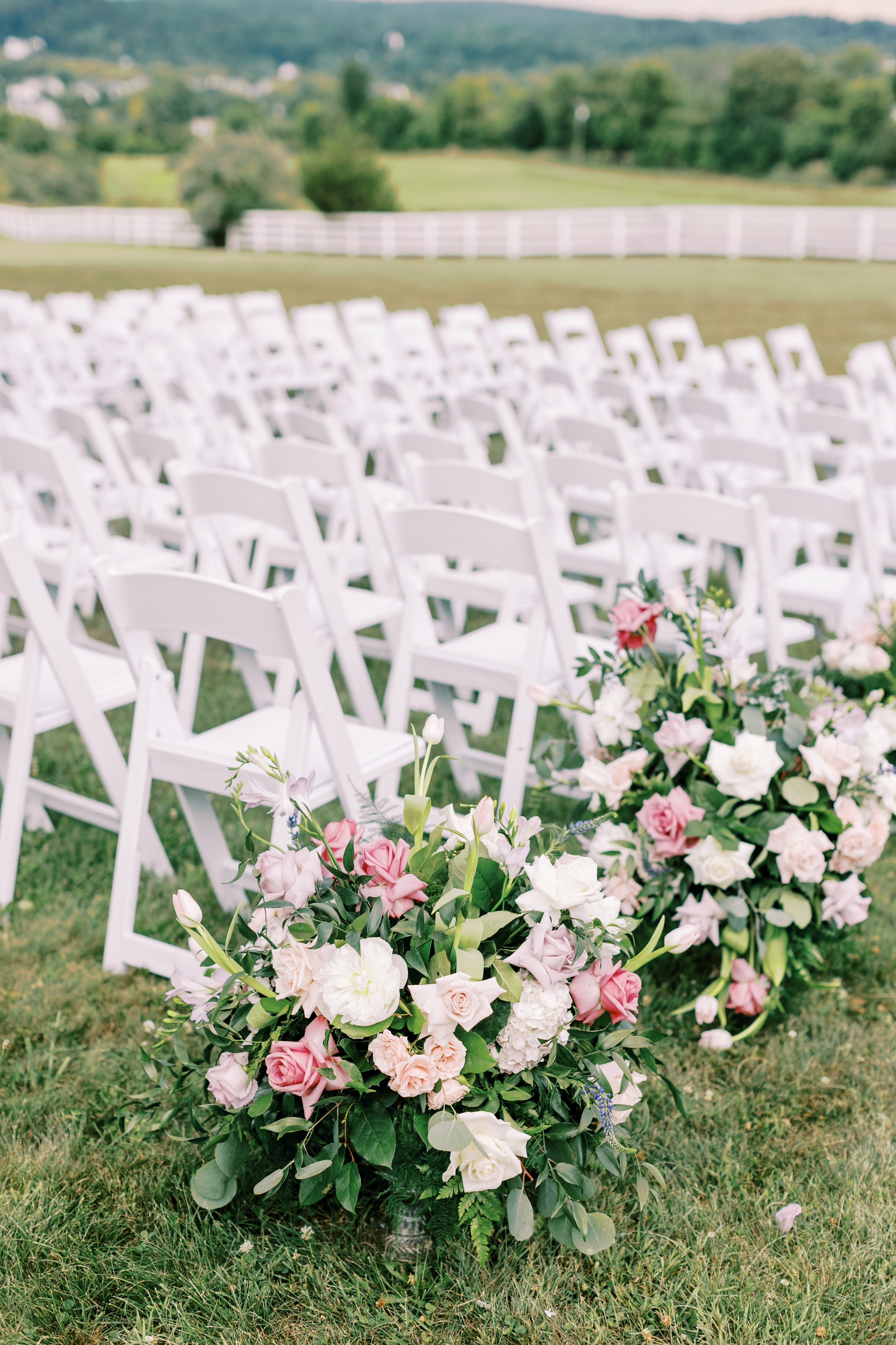 Garden roses and eucalyptus marking the end of an aisle row of white ceremony chairs