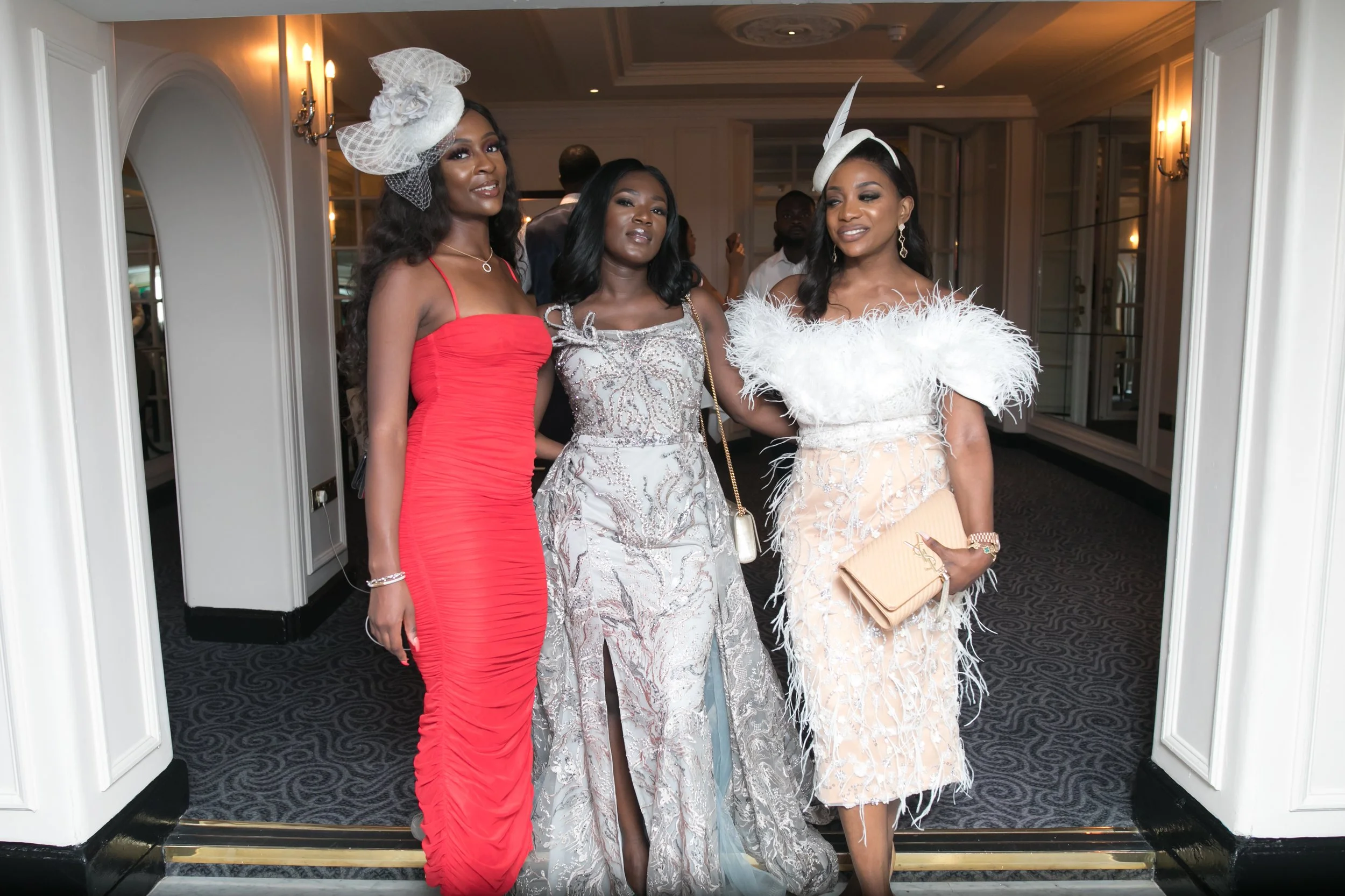 Three guests in scarlet, ivory and feathered couture in a hotel corridor