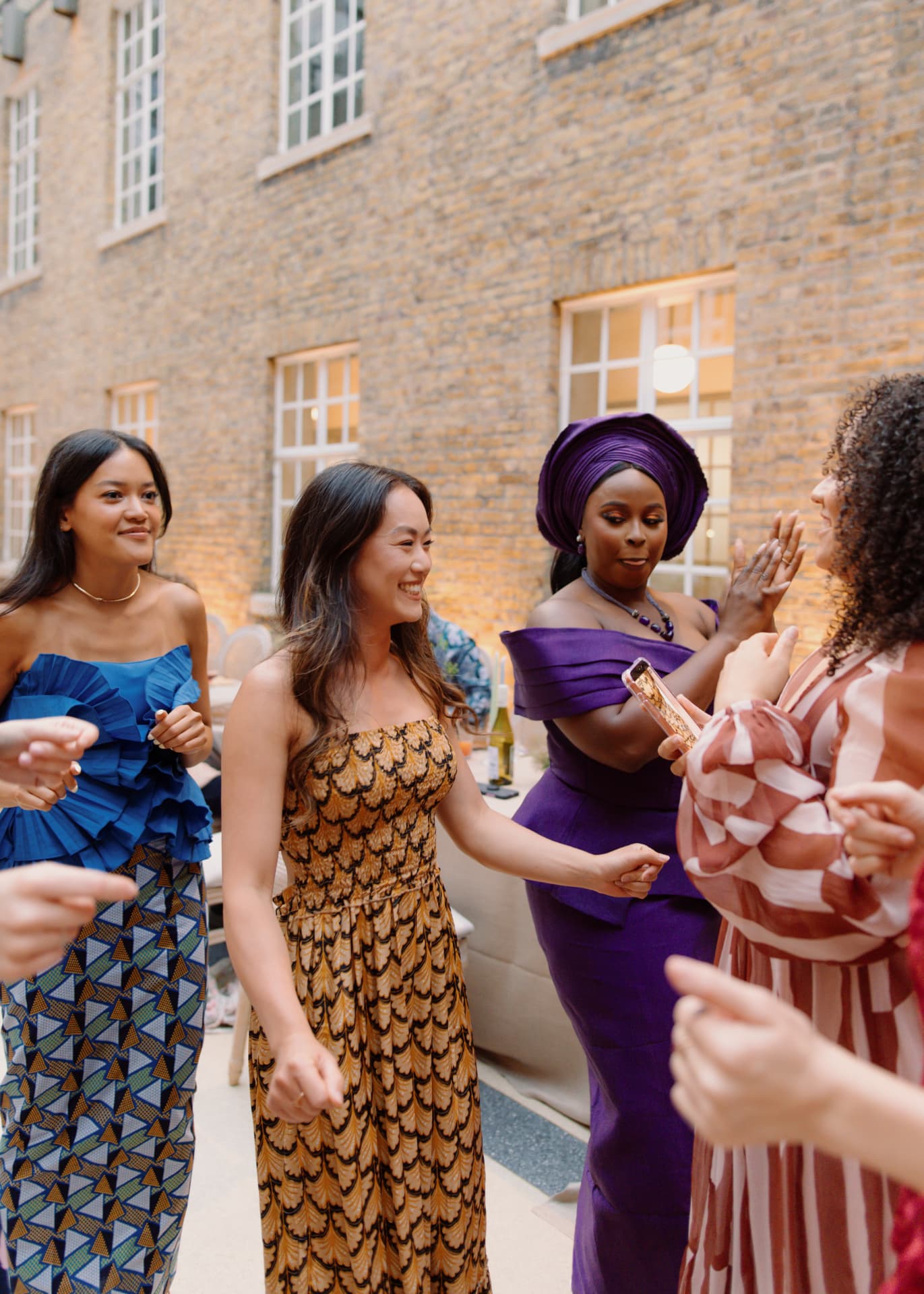 Guests in wax print, purple gele and silk dancing together in a London brick courtyard