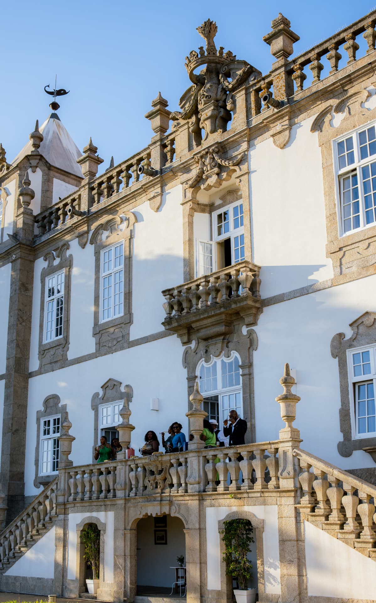Guests socialising on the ornate stone balcony of Palácio do Freixo, overlooking a baroque courtyard