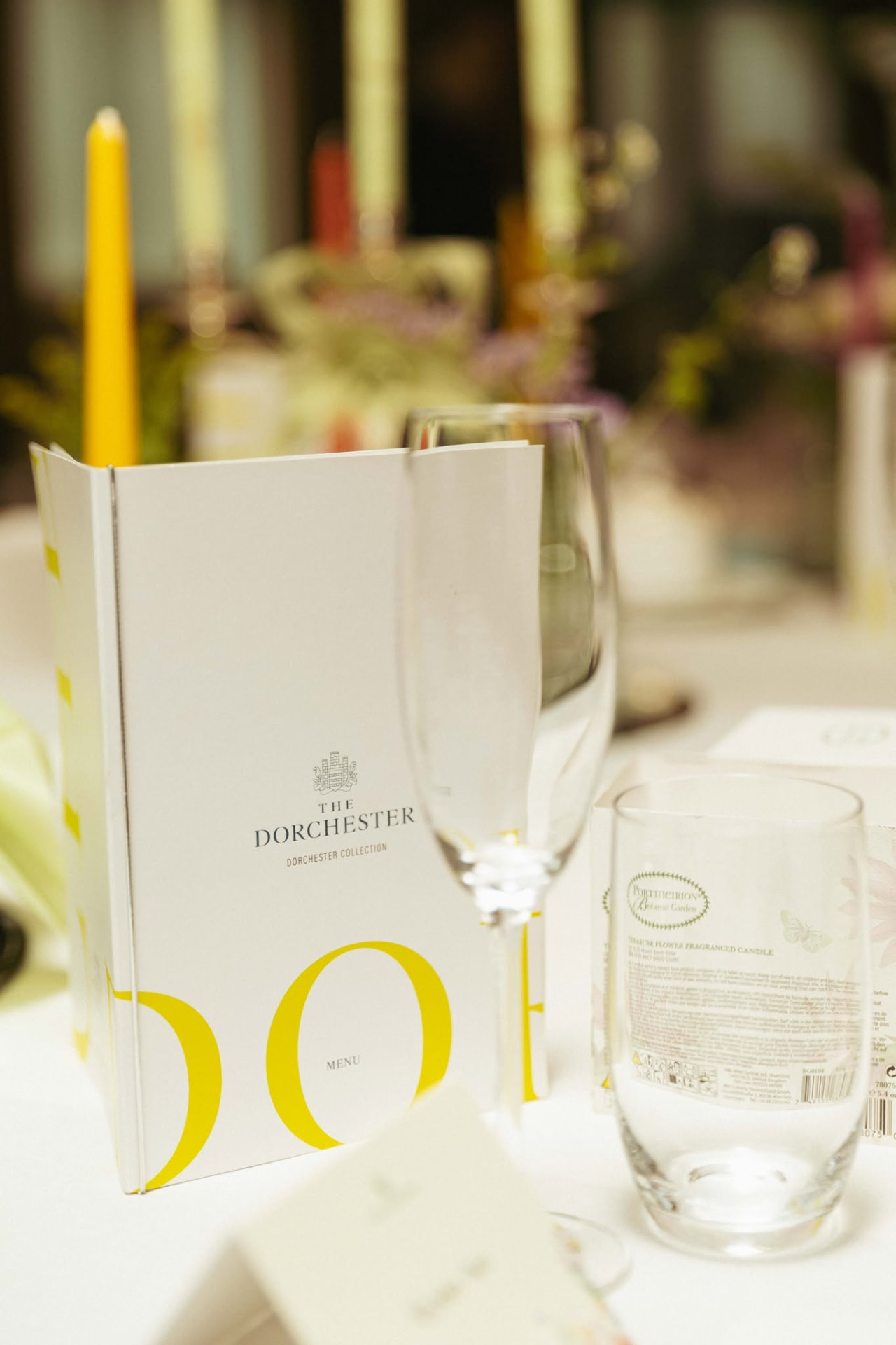 A Dorchester Collection menu card, champagne flute and candle on a dressed table
