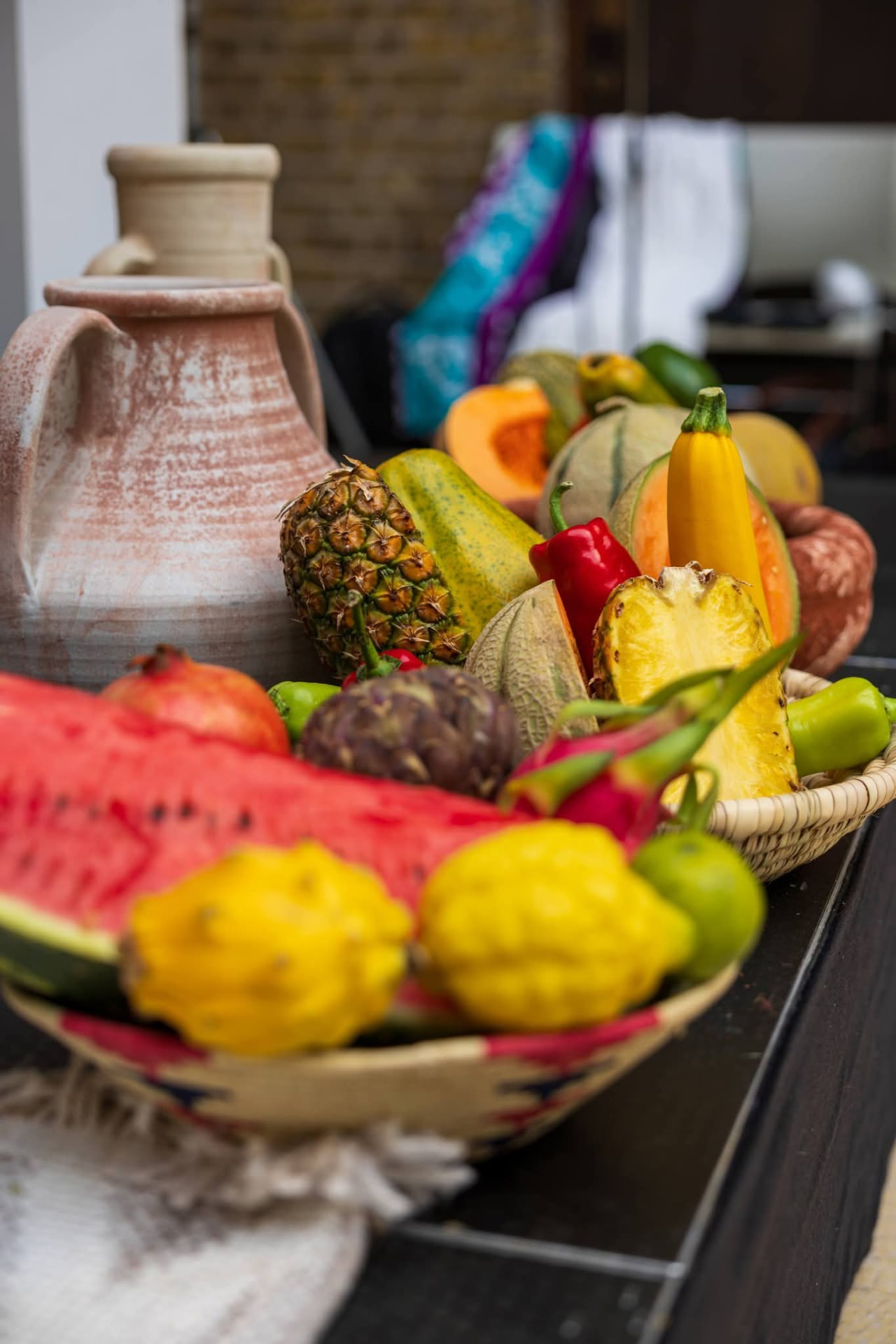 Tropical fruit still-life with ceramic vessel, watermelon, pineapple and peppers on a dark table