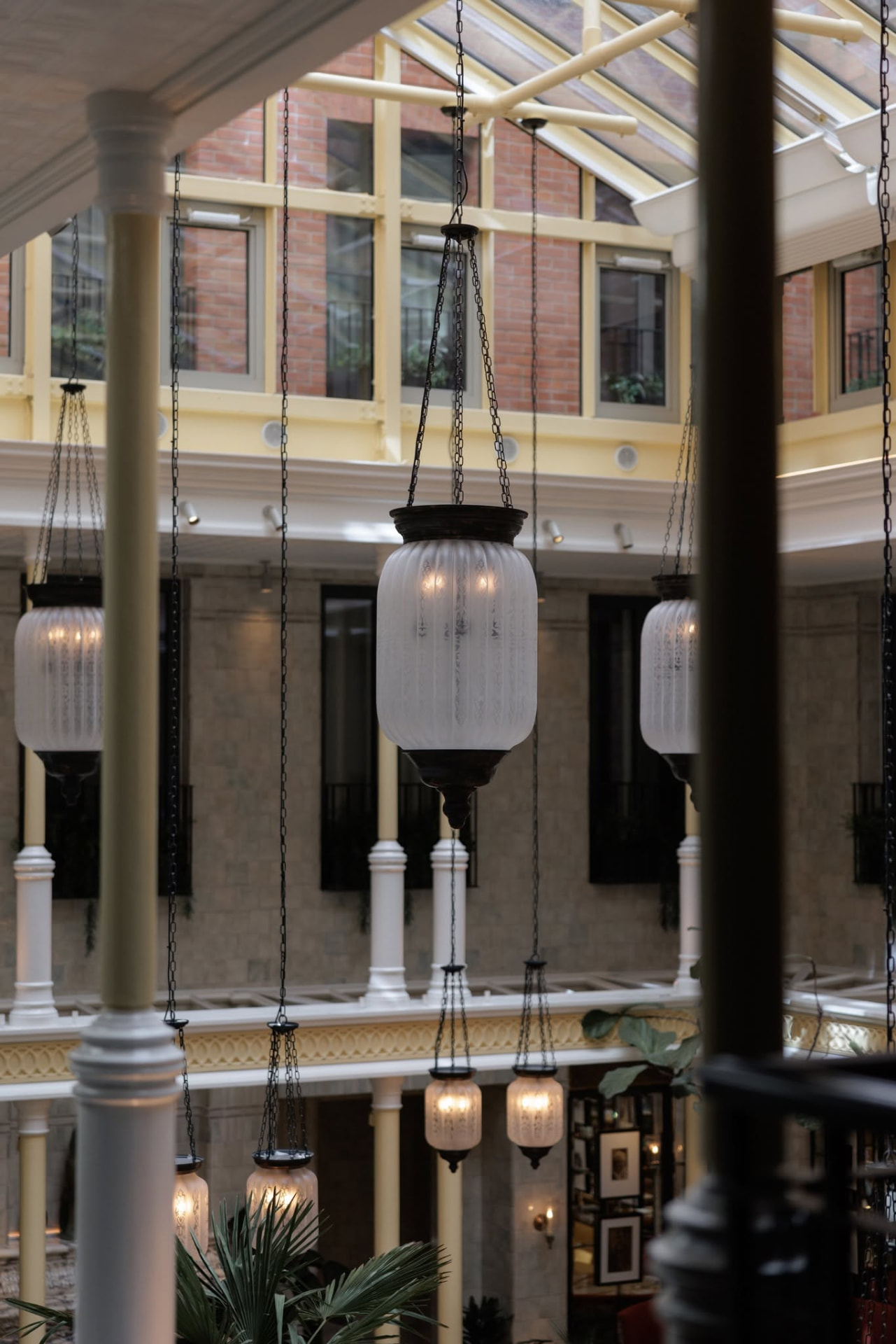 Glass roofed atrium with hanging etched glass lanterns at Nomad Hotel London