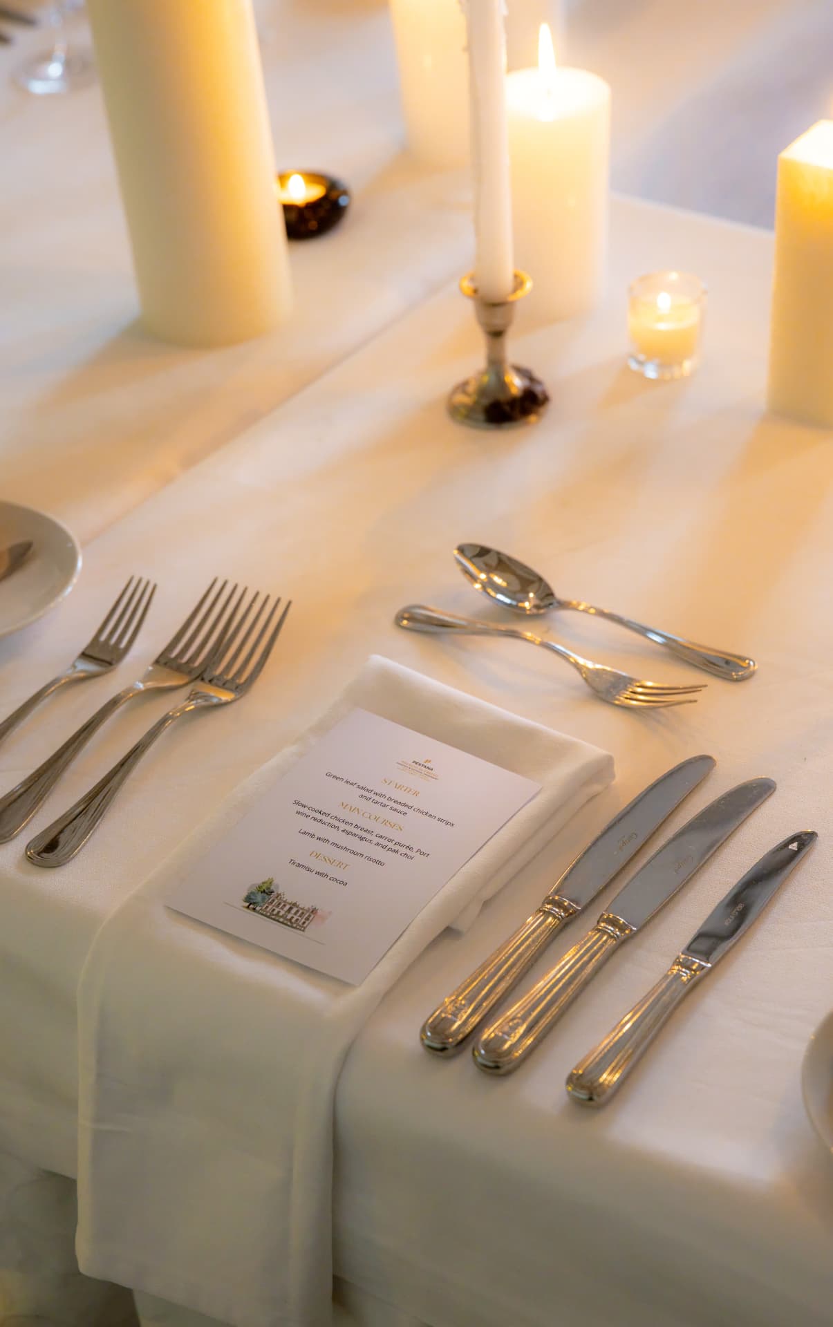 A candlelit place setting with polished silver, ivory linen and a printed Pestana menu card