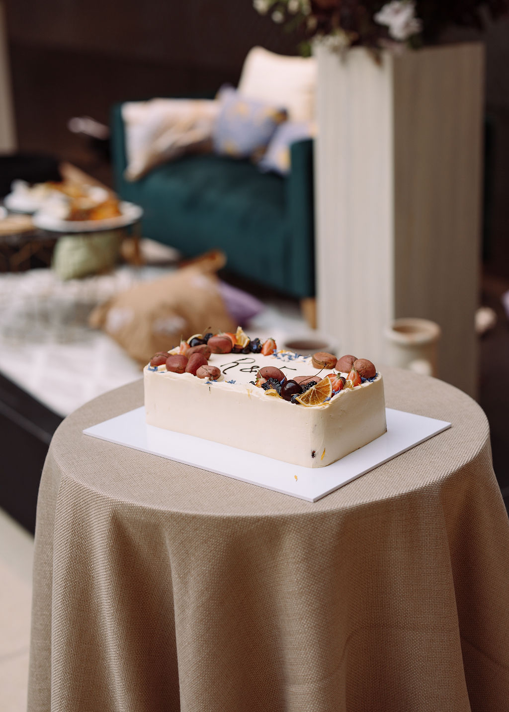 Monogrammed buttercream cake decorated with berries, dried citrus and edible flowers on a linen-draped table
