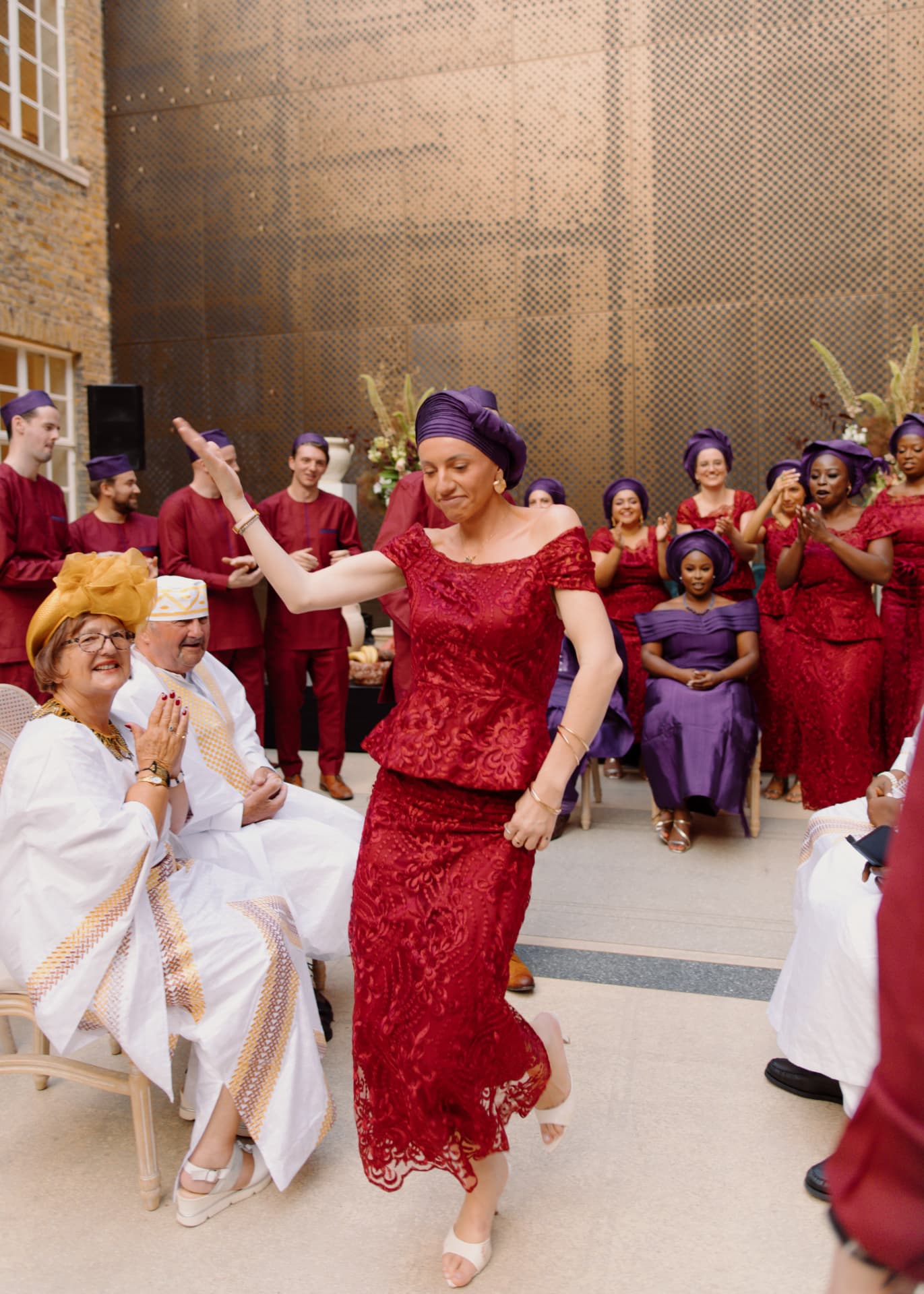 Guest in red lace dancing between seated family in a London courtyard