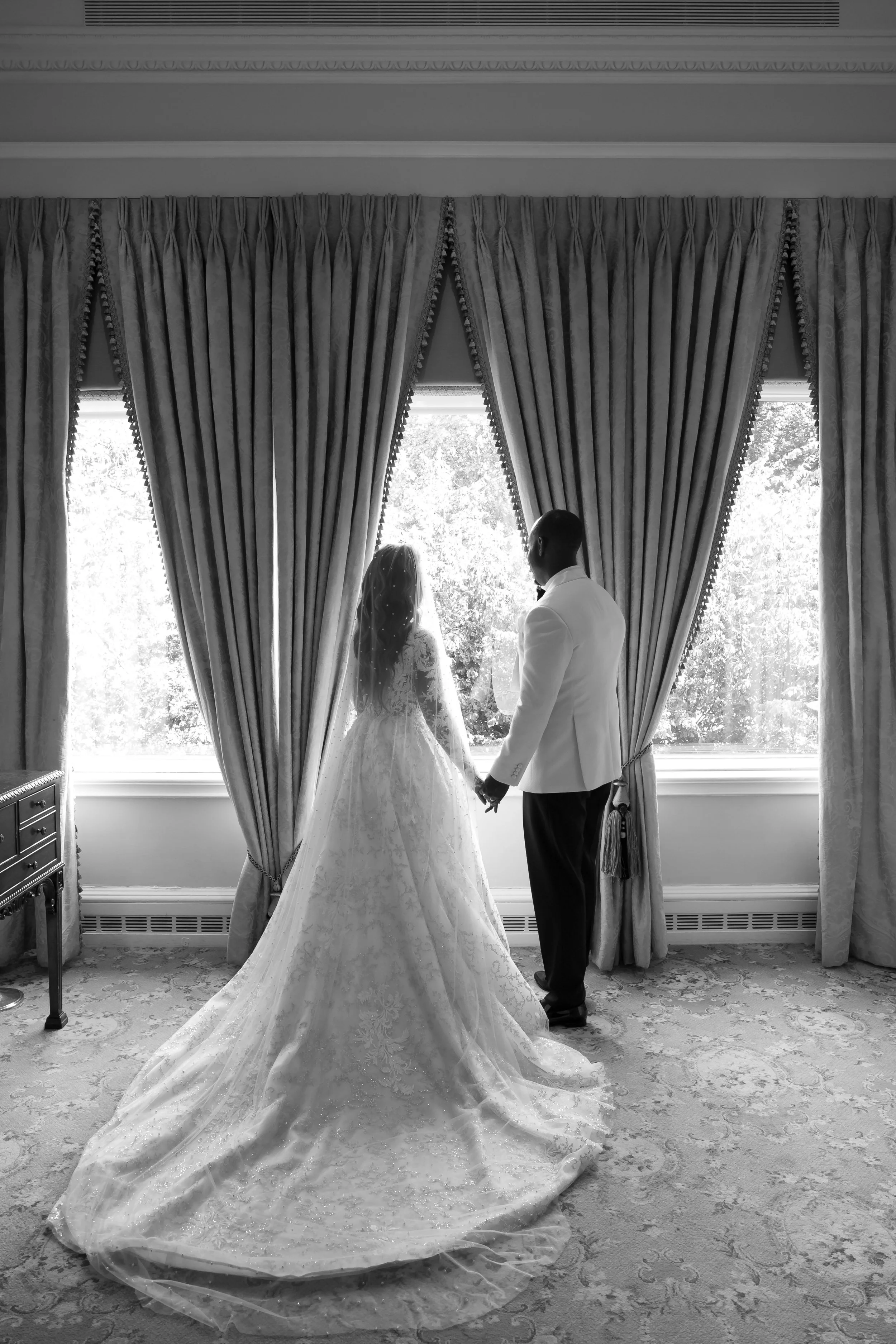 Bride and groom at a tall window, cathedral train spread across the floor, black and white