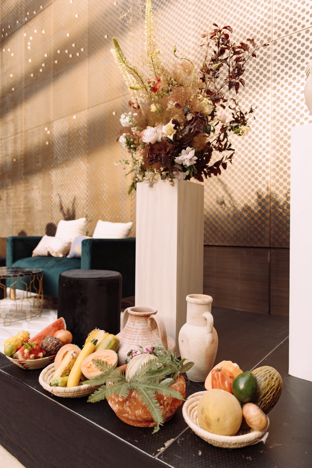 Sculptural florals, terracotta vessels and baskets of fruit beside a velvet lounge in a modern London venue