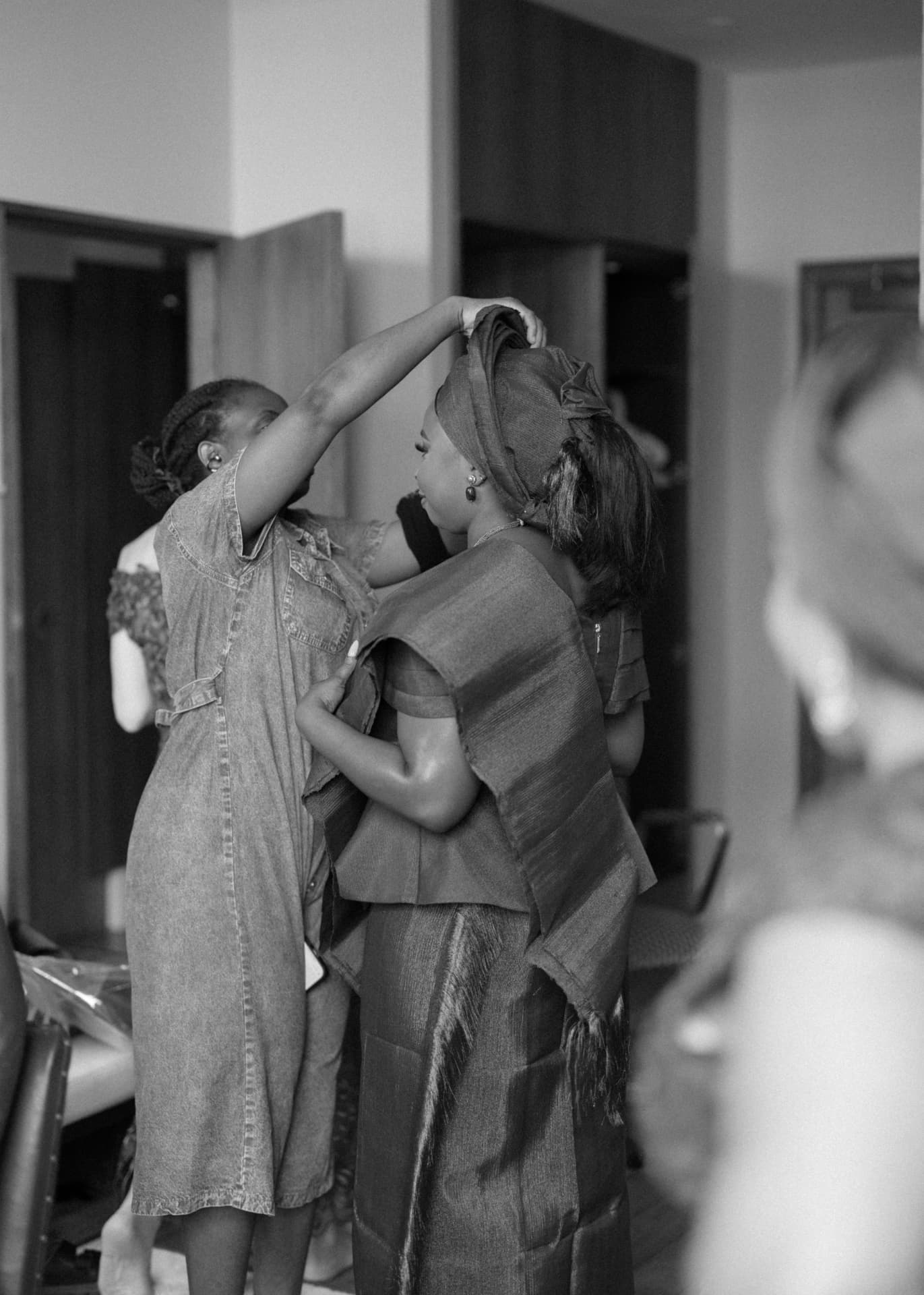A gele being tied for a guest before the ceremony, in black and white