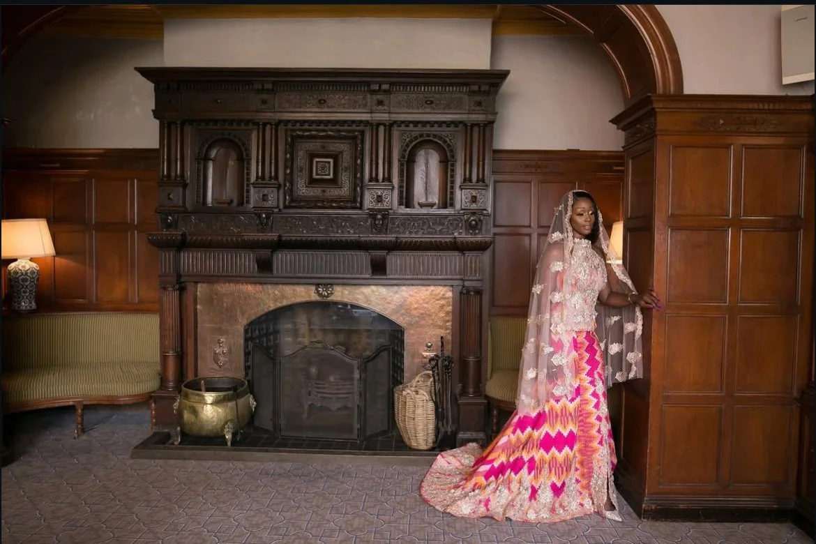 Bride in a full kente gown standing before a carved fireplace in a panelled room at The Savoy