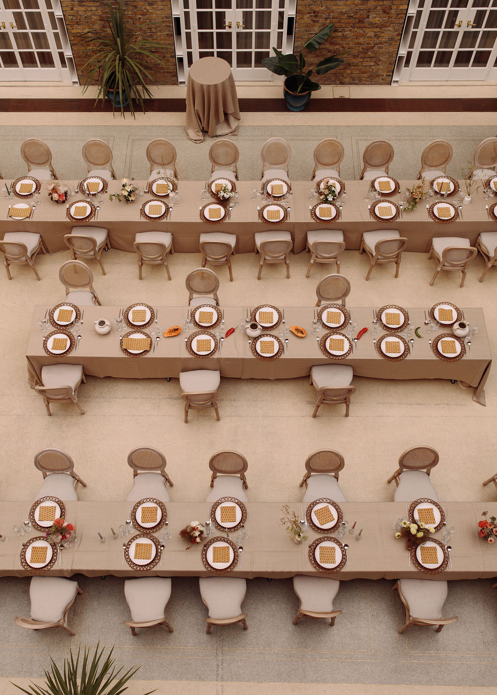 Overhead view of banquet tables laid with rattan chargers, papaya and chillies in a London courtyard