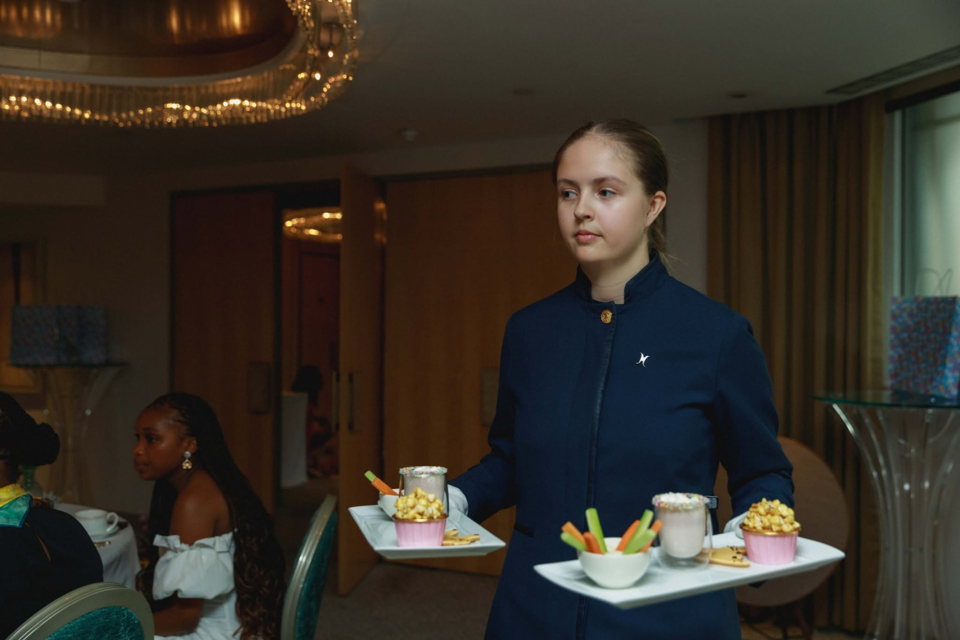 A member of hotel service staff carrying trays of afternoon tea beneath the chandelier