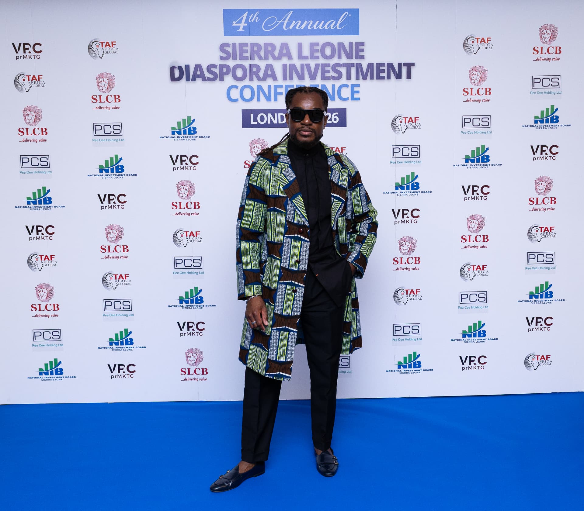 A delegate in a tailored wax-print coat photographed on the conference blue carpet