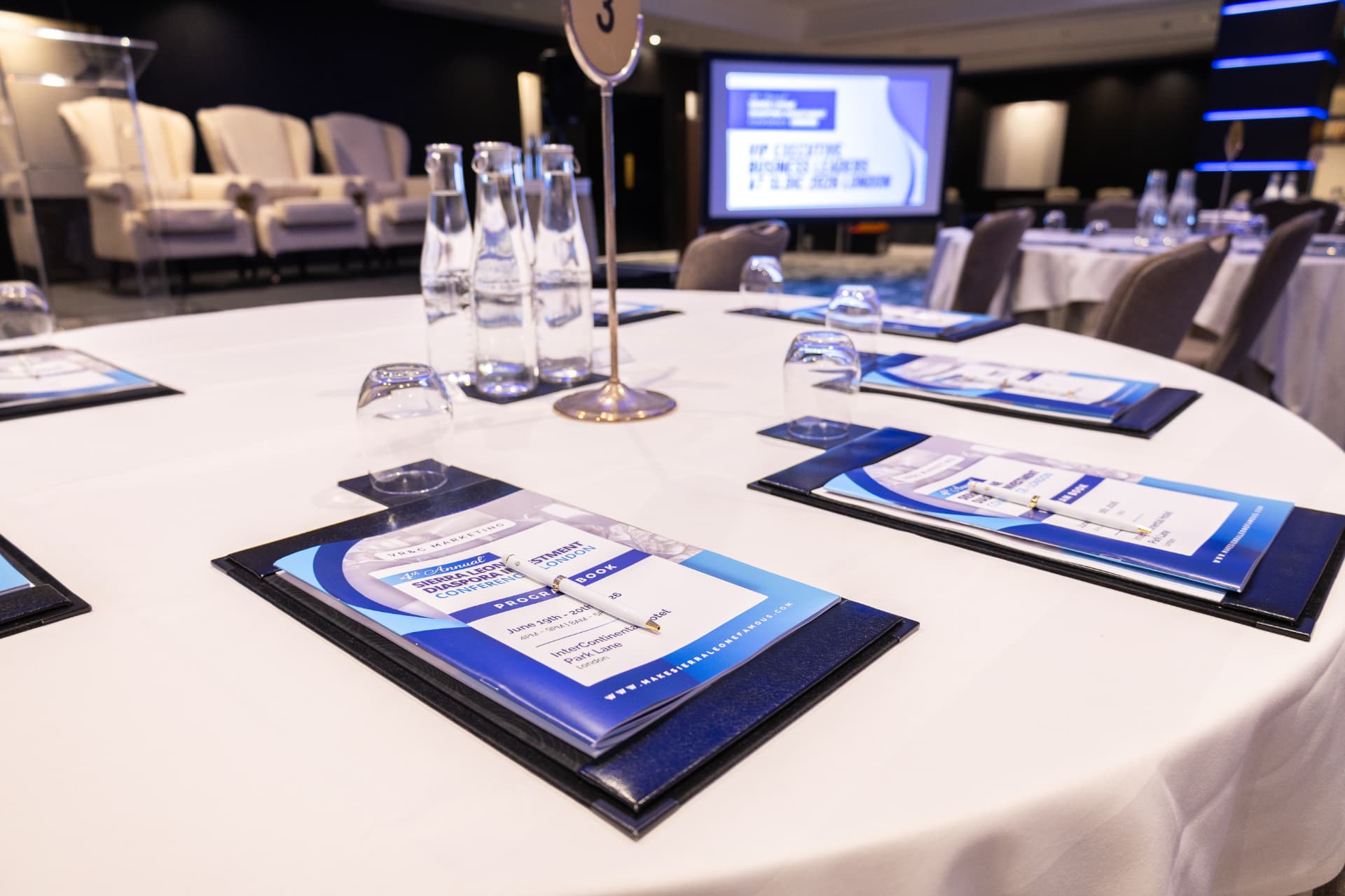 Programme books, pens and glassware laid at a round conference table